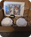 Gift box with two white flowers, a card, and a small decorative item.